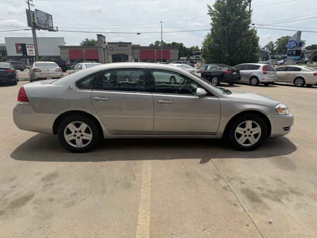 Silver four-door sedan photographed in a parking lot, with storefronts and other parked cars in the background.