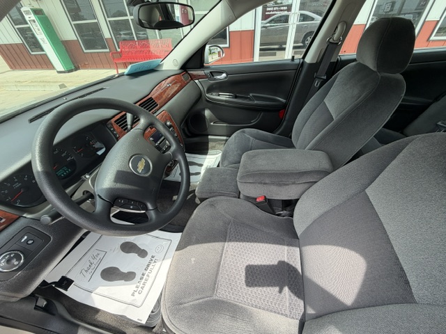 Interior view of a gray cloth-seat car cabin with wood trim, showing the steering wheel, dashboard, center console, and front seats from the driver's side to the passenger side.