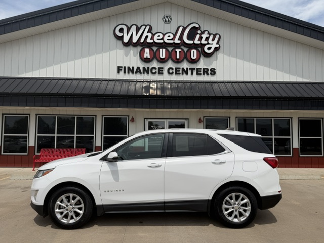 White Chevrolet Equinox SUV parked in front of Wheel City Auto Finance Centers storefront, with the dealership sign visible.