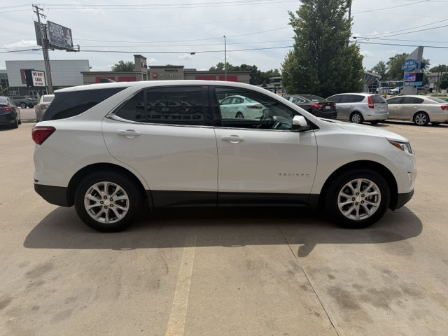Side view of a white Chevrolet Equinox SUV parked in a car dealership lot with other vehicles in the background.