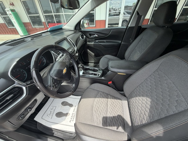 Front interior of a Chevy SUV with steering wheel, center console, gear shifter, and cloth front seats.