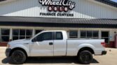 Silver Ford F-150 pickup truck parked in front of Wheel City Auto Finance Centers storefront.