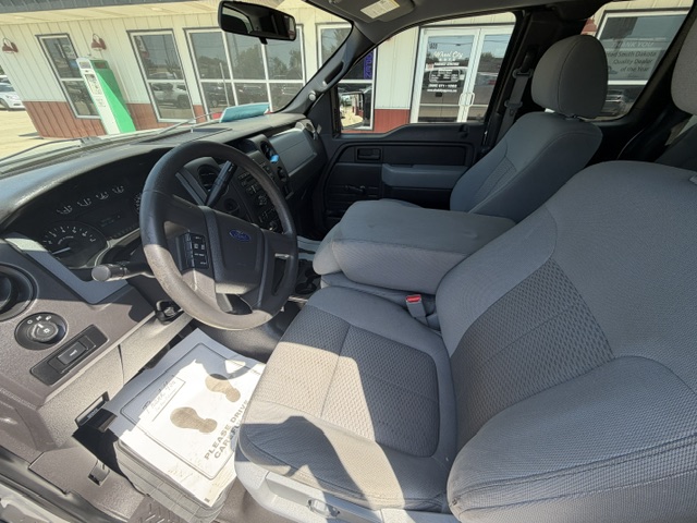 Interior of a gray pickup truck: driver seat, steering wheel, and front passenger seat seen from the driver's side.