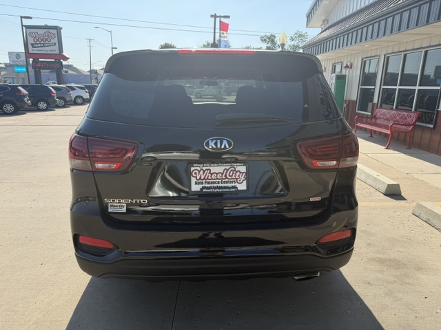 Rear view of a black Kia Sorento SUV parked at a dealership lot, with WheelCity Auto Finance Centers on the license plate frame.
