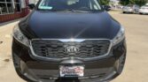 Front view of a black Kia SUV parked at a dealership, with Wheel City Auto Finance plate frame and a building to the left.