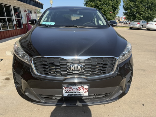 Front view of a black Kia SUV parked at a dealership, with Wheel City Auto Finance plate frame and a building to the left.