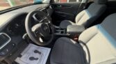 Front interior of a gray cloth Kia sedan, showing the steering wheel, dashboard, center console, and front seats bathed in sunlight.