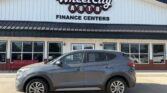 Gray SUV parked in front of Wheel City Auto Finance Centers dealership with a white façade, black awning, and large display windows.