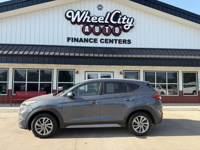 Gray SUV parked in front of Wheel City Auto Finance Centers dealership with a white façade, black awning, and large display windows.