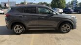 Gray SUV parked in a car lot on a sunny day, side profile visible, with other cars in the background.