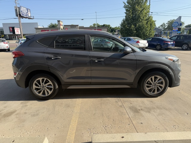 Gray SUV parked in a car lot on a sunny day, side profile visible, with other cars in the background.