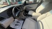 Light gray car interior showing the front seats, steering wheel, dashboard, and center console; driver's door open and paper floor mat visible.