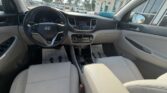 Interior view of a beige Hyundai car: front seats, steering wheel, center stack with touchscreen, and dashboard seen from the back seat as daylight comes through the windows.