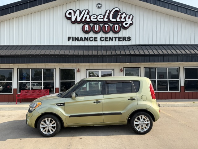 Beige compact car parked in front of Wheel City Auto Finance Centers storefront with large signage above.
