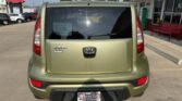 Rear view of an olive-green Kia Soul in a dealership lot, with a Wheel City license plate frame and a back window sticker visible.