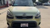 Front view of a light olive Kia SUV parked in a dealership lot, with a Wheel City license plate frame.