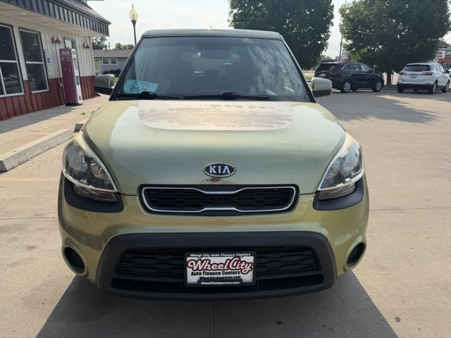 Front view of a light olive Kia SUV parked in a dealership lot, with a Wheel City license plate frame.