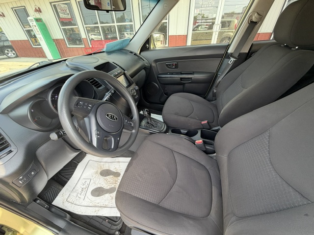Interior of a Kia car from the driver's side: steering wheel, dashboard, center console, two front seats, door panel, and a floor mat with footprints visible