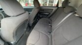 Interior of a car showing a gray fabric rear bench seat for three, with headrests and seat belts; front seats visible, car door panels, and windows revealing a dealership exterior in the background.