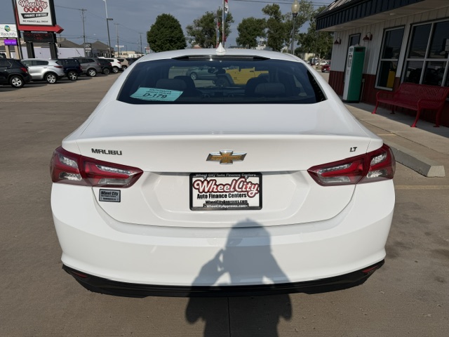 Rear view of a white Chevrolet Malibu LT at a car dealership, with Wheel City license plate frame and a price tag visible in the rear window.