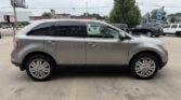 Side view of a silver mid-size SUV with chrome wheels parked in a dealership lot and tinted windows.