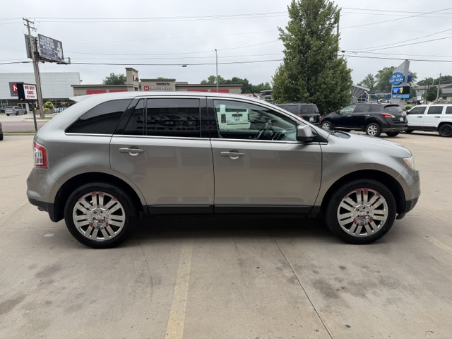 Side view of a silver mid-size SUV with chrome wheels parked in a dealership lot and tinted windows.