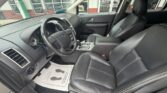 Interior of a black-leather Ford SUV showing the driver's area with steering wheel, dashboard, and center console; front passenger seat beside it, all in clean condition as seen from the open driver-side door in a dealership lot.