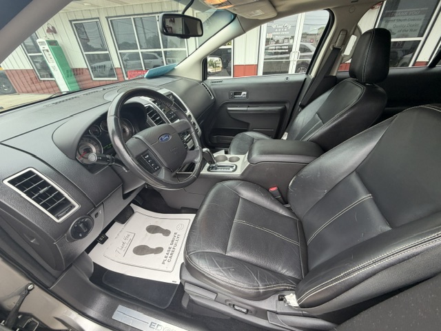 Interior of a black-leather Ford SUV showing the driver's area with steering wheel, dashboard, and center console; front passenger seat beside it, all in clean condition as seen from the open driver-side door in a dealership lot.