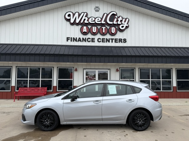 Silver sedan parked in front of Wheel City Auto Finance Centers storefront at a car dealership.