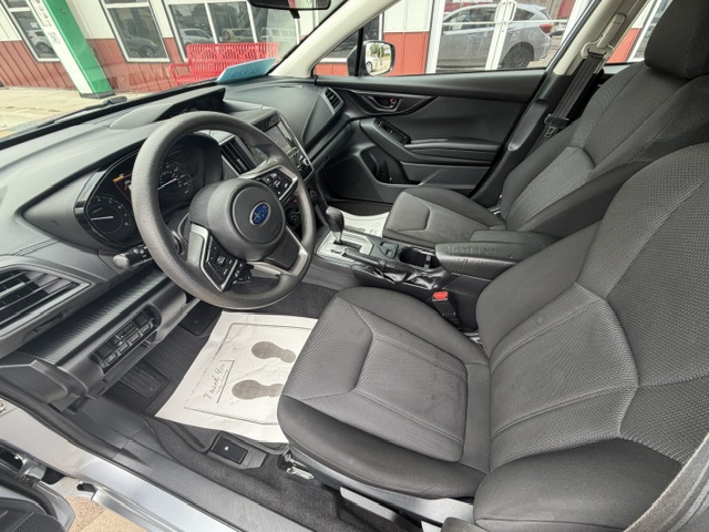 Front interior of a sedan showing the driver’s seat, steering wheel, and center console with the gear shifter and cup holders.