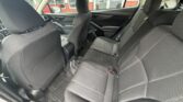 Interior of a car viewed from the rear passenger side, showing a dark cloth three-seat back bench with headrests, front seats, center console, and rubber floor mats.