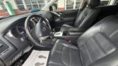 Front interior of a black leather SUV showing the dashboard, steering wheel, center console, gear shifter, and both front seats; a floor mat with footprints is visible on the driver’s side.