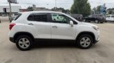 Side view of a white compact SUV parked in a lot, with black lower trim and silver alloy wheels, and other vehicles and shops in the background.