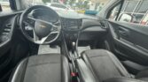 Black leather sedan interior photographed from the back seat, showing the steering wheel with a Chevrolet emblem and the center console. It includes a touchscreen display and gear shifter between two front seats.