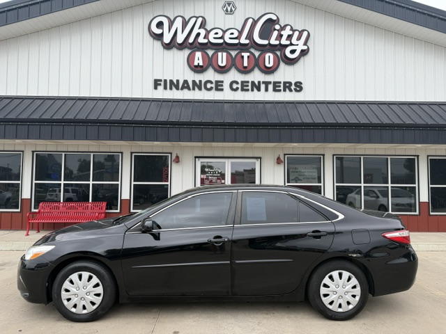 Black four-door sedan parked in front of Wheel City Auto Finance Centers storefront, signage visible above the building front.