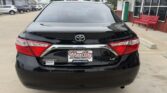 Rear view of a black Toyota Camry LE at a dealership, license plate frame reads Wheel City Auto Finance Center