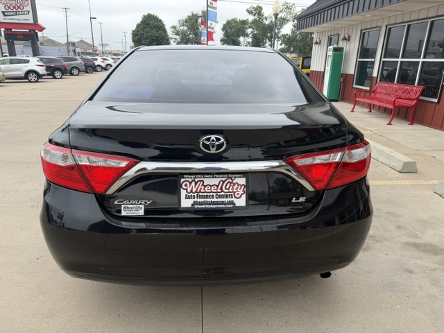 Rear view of a black Toyota Camry LE at a dealership, license plate frame reads Wheel City Auto Finance Center