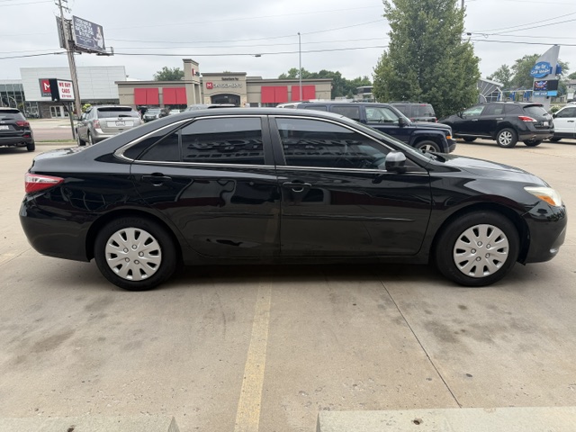 Black four-door sedan parked in a dealership lot with other cars and storefronts in the background, side view. (Informative)