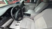 Interior view of a Toyota Camry from the driver’s side, showing the steering wheel, dashboard, center console, and light gray cloth seats. A paper floor mat with footprints rests on the driver’s side.