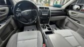 Inside a gray Toyota sedan: steering wheel, center touchscreen, cupholders, and light gray fabric seats at the front.