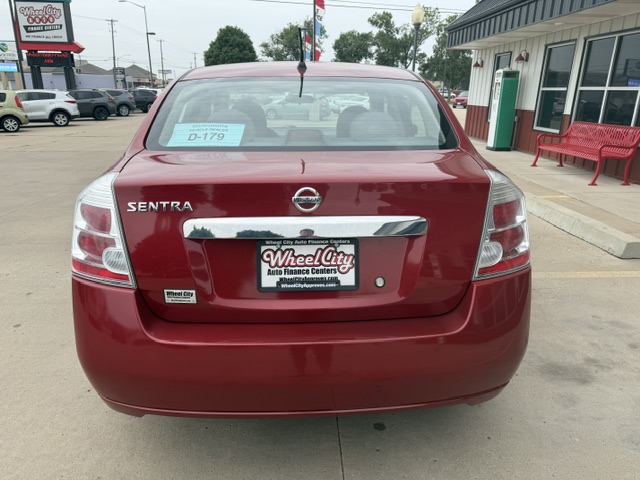 Rear view of a red Nissan Sentra in a dealership lot, with a Wheel City license plate frame and a price sticker on the rear window.