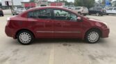 Side view of a red four-door sedan parked in a parking lot, showing the car's profile and hubcaps.