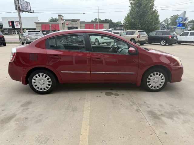 Side view of a red four-door sedan parked in a parking lot, showing the car's profile and hubcaps.