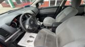 Interior of a gray sedan: driver and front passenger seats, black dashboard, steering wheel with emblem, gear shifter, center console, and floor mats outside view through the door frame