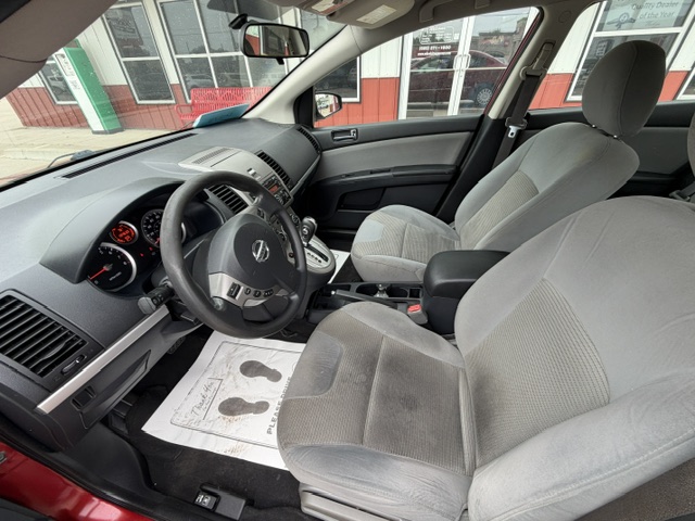 Interior of a gray sedan: driver and front passenger seats, black dashboard, steering wheel with emblem, gear shifter, center console, and floor mats outside view through the door frame