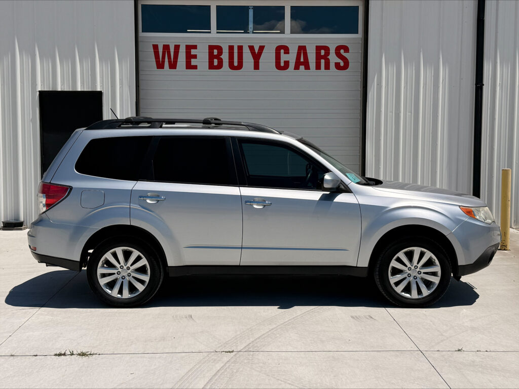 Silver SUV parked in front of a building with a large 'WE BUY CARS' sign above the doorway, empty lot.