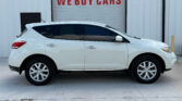 White SUV parked in front of a building with a large 'WE BUY CARS' sign on a gray garage door behind it.