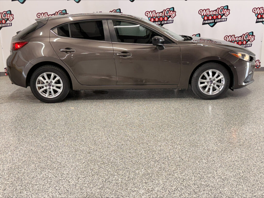 Side profile of a gray crossover SUV parked indoors with Wheel City Auto branding in the background.