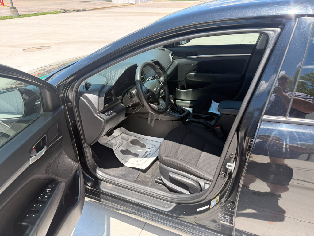 Open driver's-side door of a dark SUV, showing the steering wheel, dashboard, and center console in daylight.