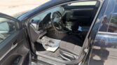 Open driver's-side door of a dark SUV, showing the steering wheel, dashboard, and center console in daylight.
